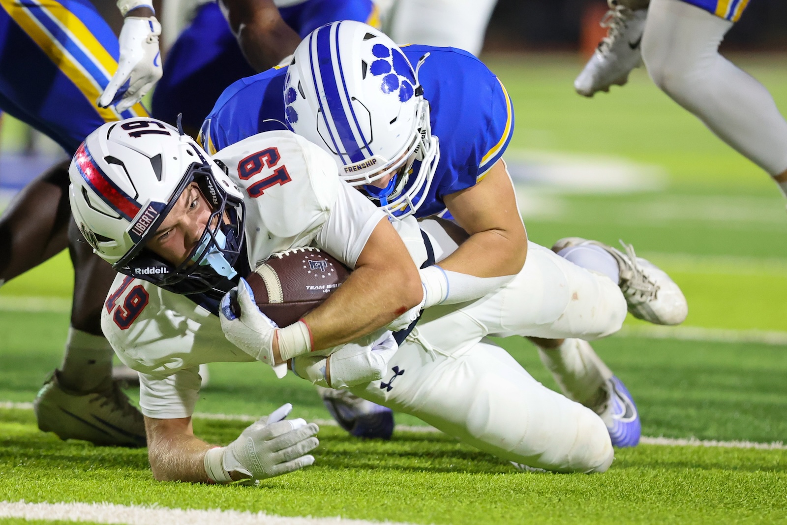 Seabolt Chase-18268 | Press Pass Sports Football player in white dives with the ball as a blue-jersey defender tackles him on a green field.