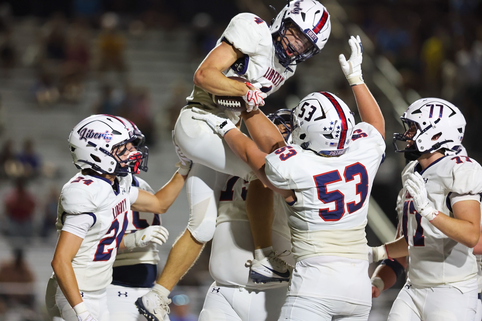 Seabolt Chase-18352 | Press Pass Sports Football players from Liberty lift a teammate in celebration on the field at night.