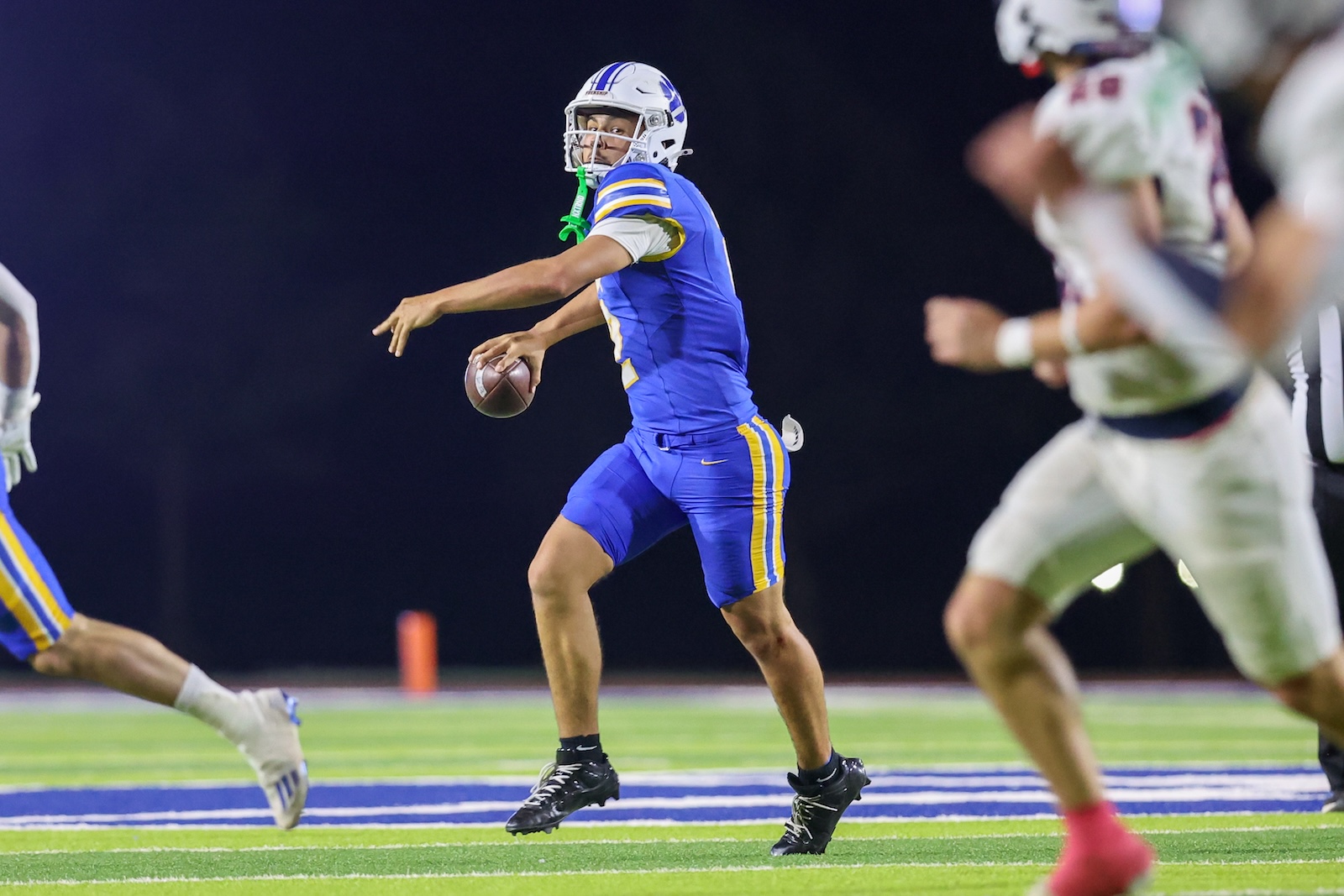 Seabolt Chase-18740 | Press Pass Sports Quarterback in blue and yellow uniform throws a pass on a night football game on a green field.