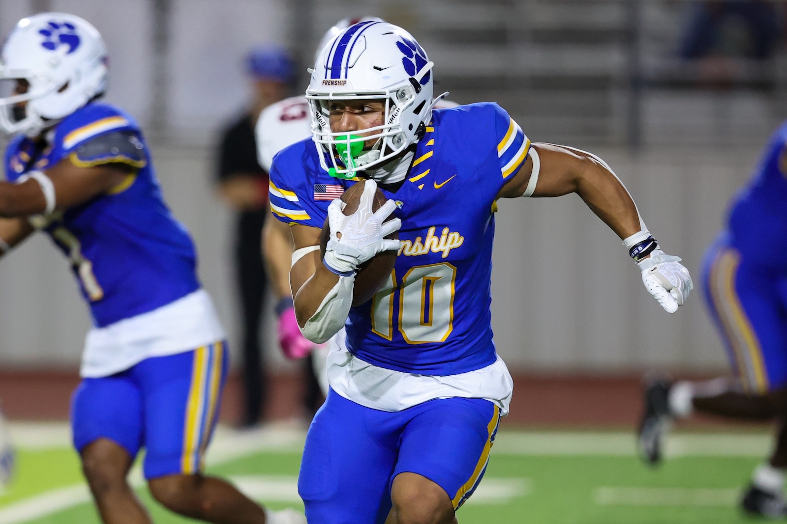 Seabolt Chase-19239 | Press Pass Sports Football player in blue and gold uniform runs with the ball during a game, clearly wearing #10 on the jersey and a white helmet with a blue paw print logo.