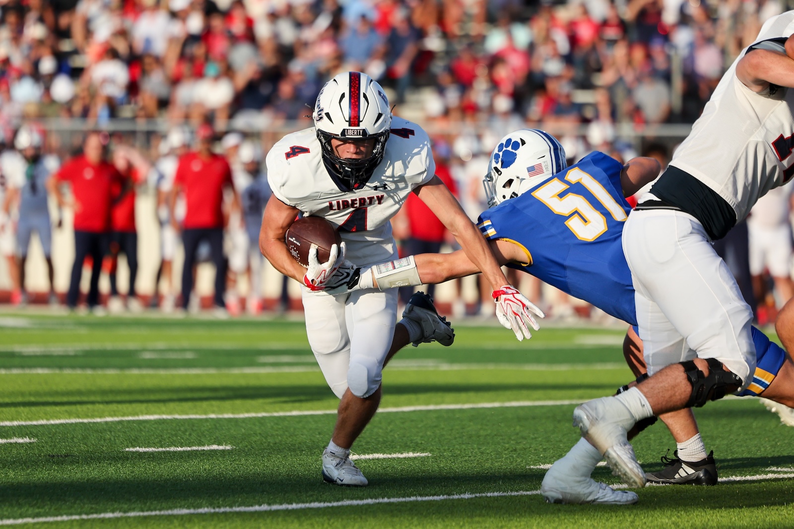 Seabolt Chase-25179 | Press Pass Sports Liberty player carries the ball while a defender in blue reaches in for a tackle during a college football game.