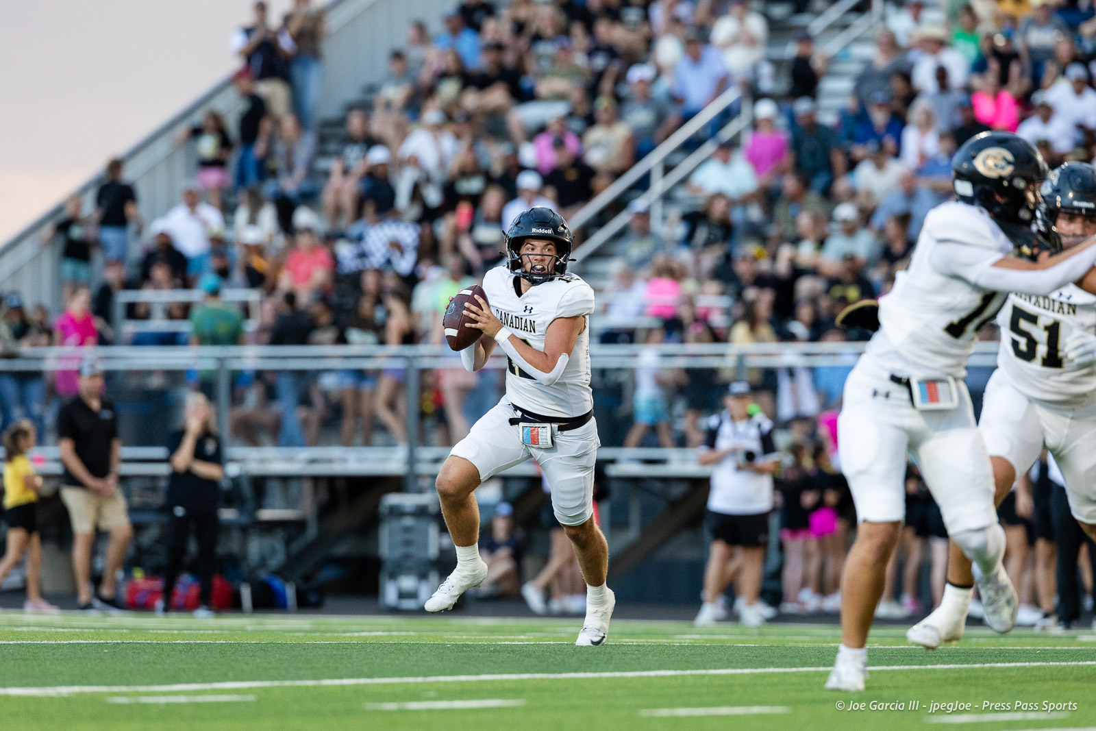 Canadian football player in a white jersey runs with the ball during a game, with a crowded stadium behind.