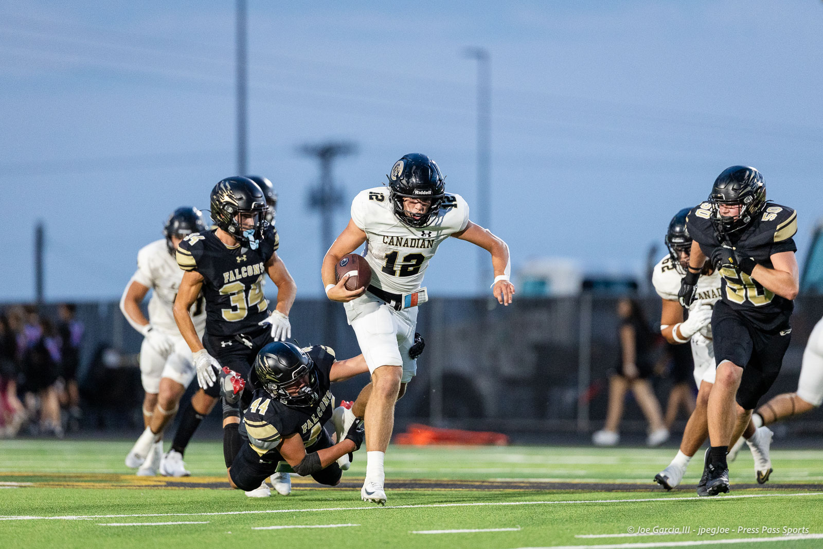 Canadian football player in white, number 12, runs with the ball as Falcons defenders pursue on a green turf field.