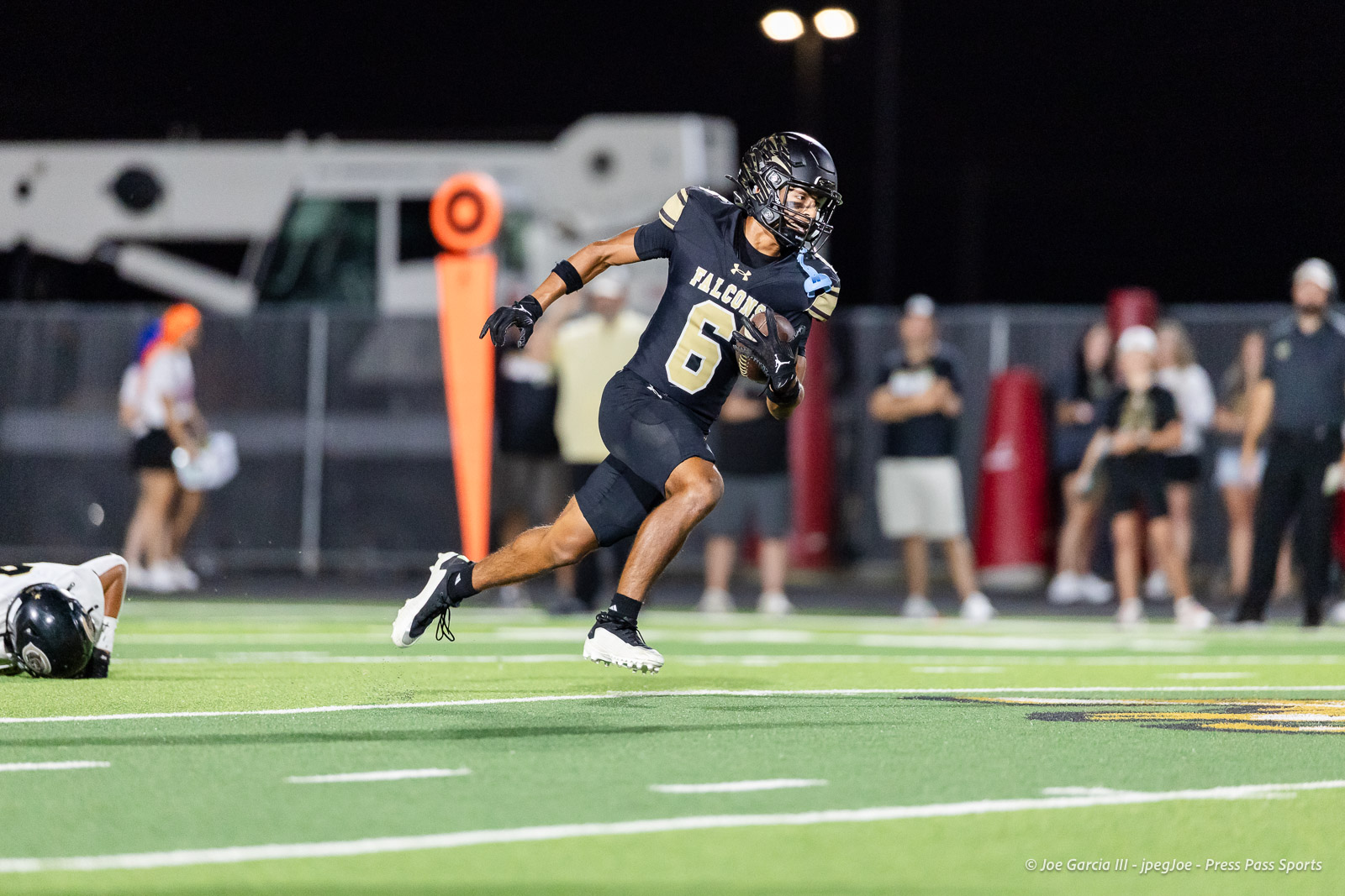 Falcons player wearing #6 runs with the ball on a green turf at night; blurred crowd and sideline in the background