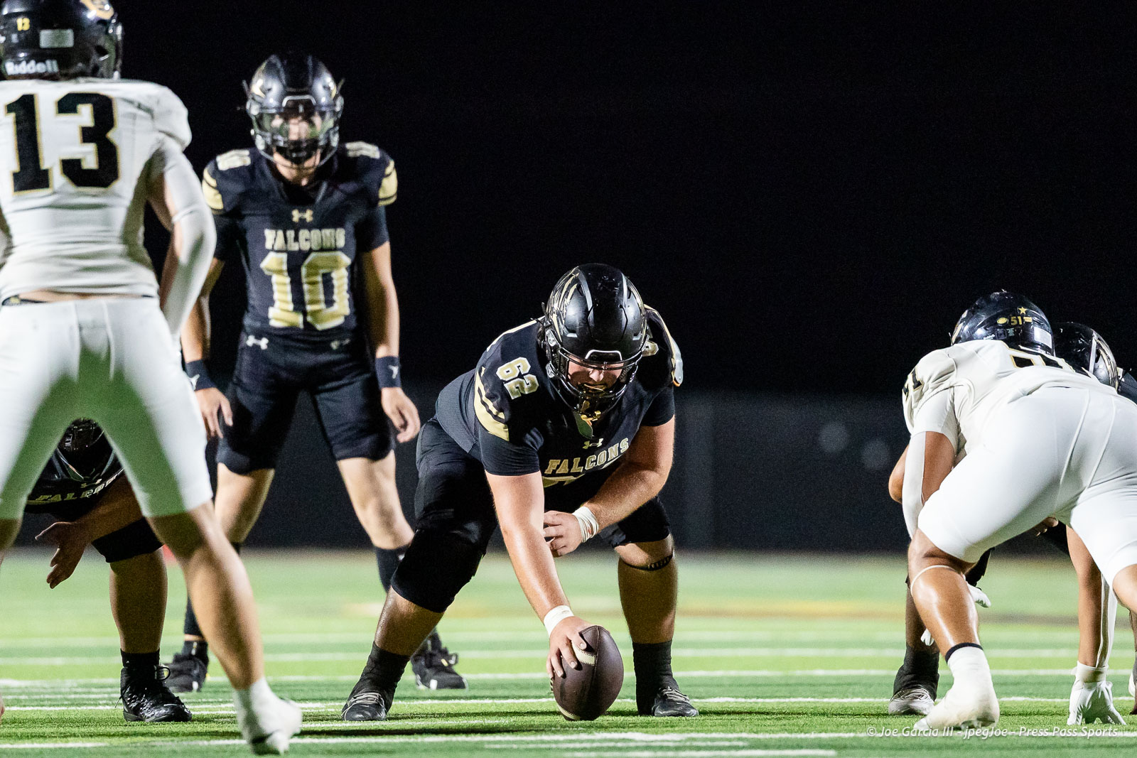 Falcons center in black uniform snaps the ball during a nighttime football game with linemen ready at the line of scrimmage.