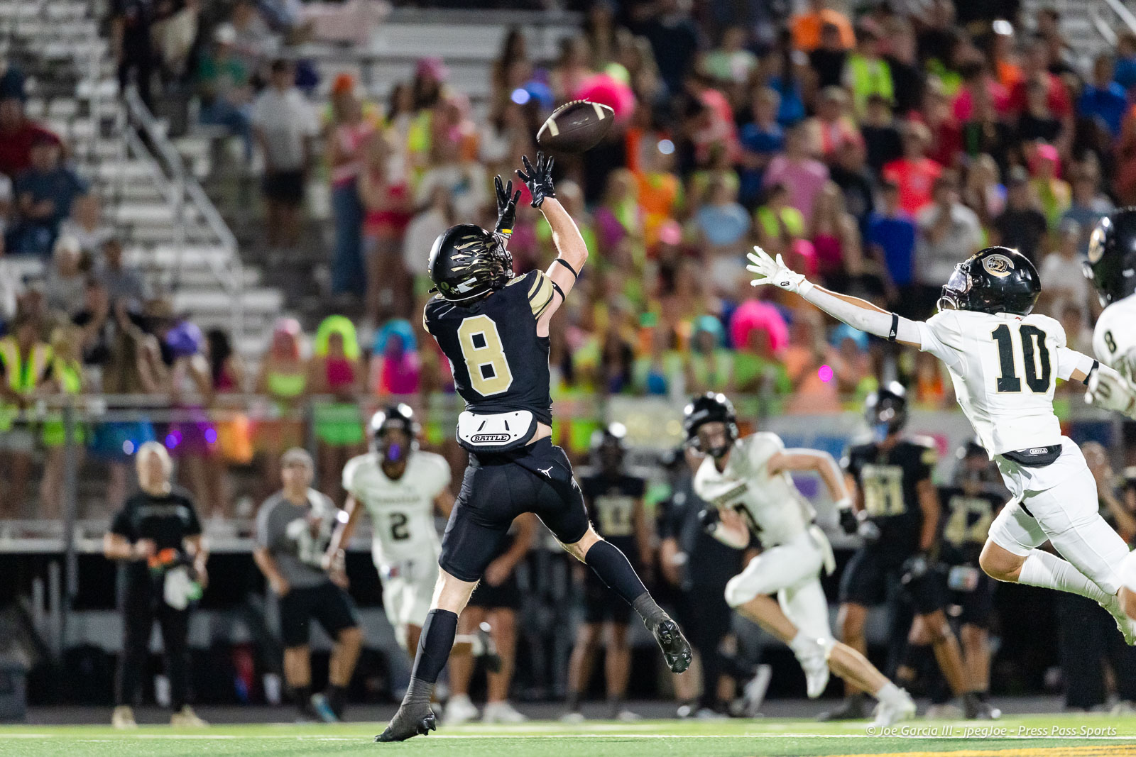 Football player in dark jersey (#8) leaps to catch the ball as defenders close in on a crowded stadium backdrop.