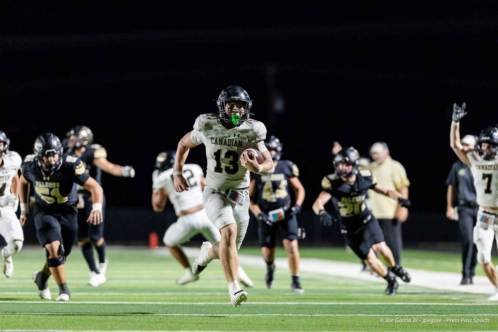 Canadian football player wearing number 13 in white runs with ball down the field at night, pursued by opponents.