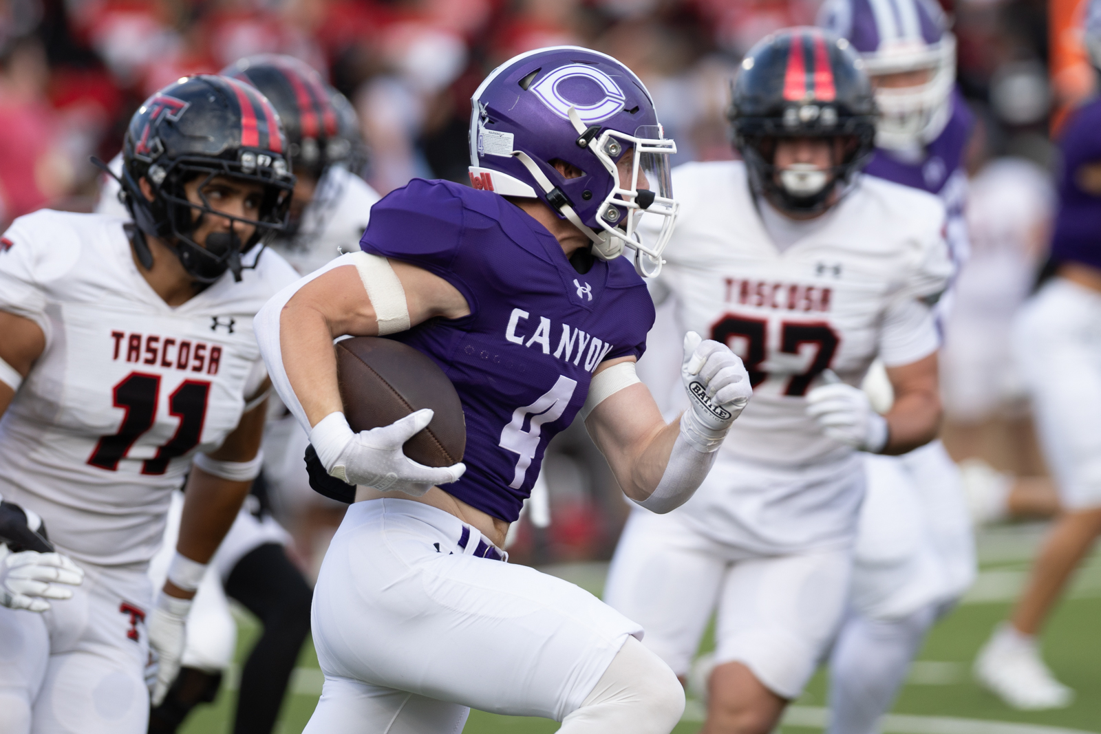 THS-CHS-FB-5 | Press Pass Sports Running back in a purple Canyon uniform with number 4 sprints with the football, white-clad defenders in pursuit on a football field.