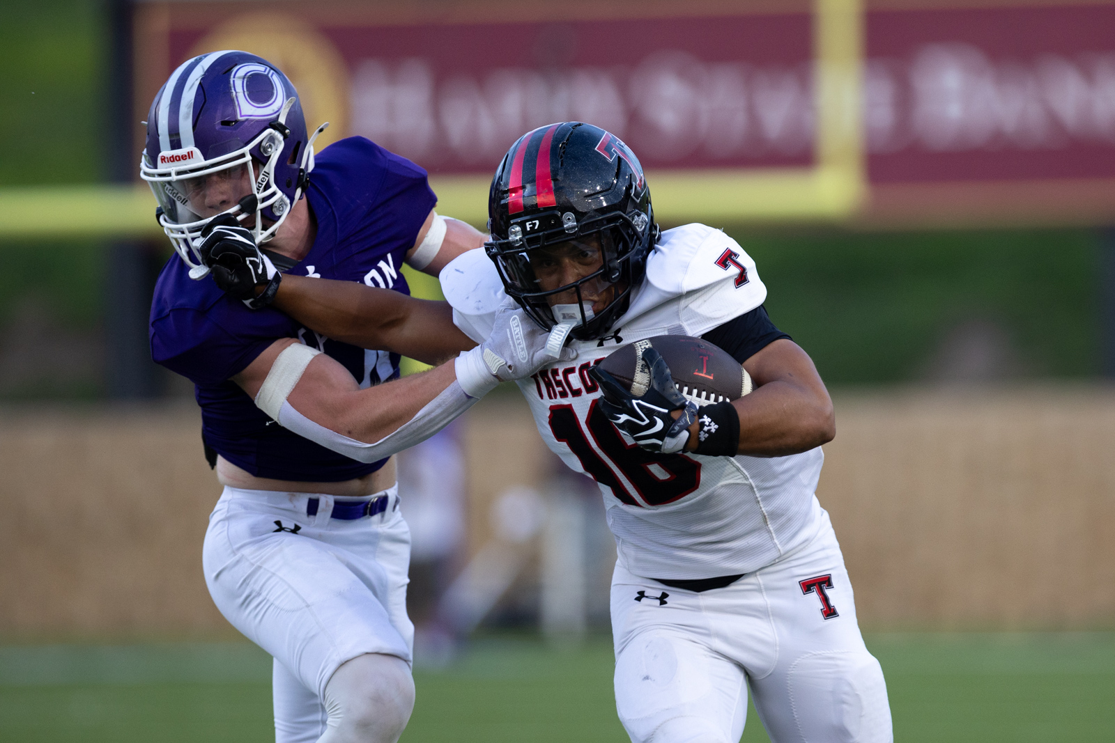 THS-CHS-FB-20 | Press Pass Sports Two football players collide as a ball carrier in white uniform runs with the ball while a defender in purple wraps his arm around him.