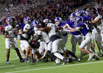 THS-CHS-FB-42 | Press Pass Sports Football players collide at the line of scrimmage during a nighttime game, white and purple uniforms in a tight scrum.