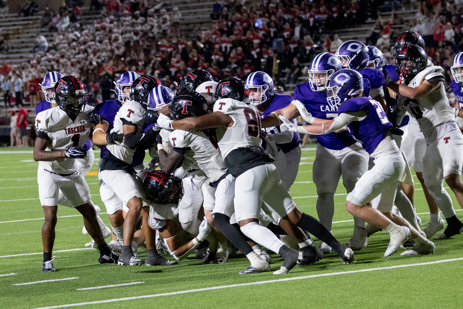 THS-CHS-FB-42 | Press Pass Sports Football players collide at the line of scrimmage during a nighttime game, white and purple uniforms in a tight scrum.