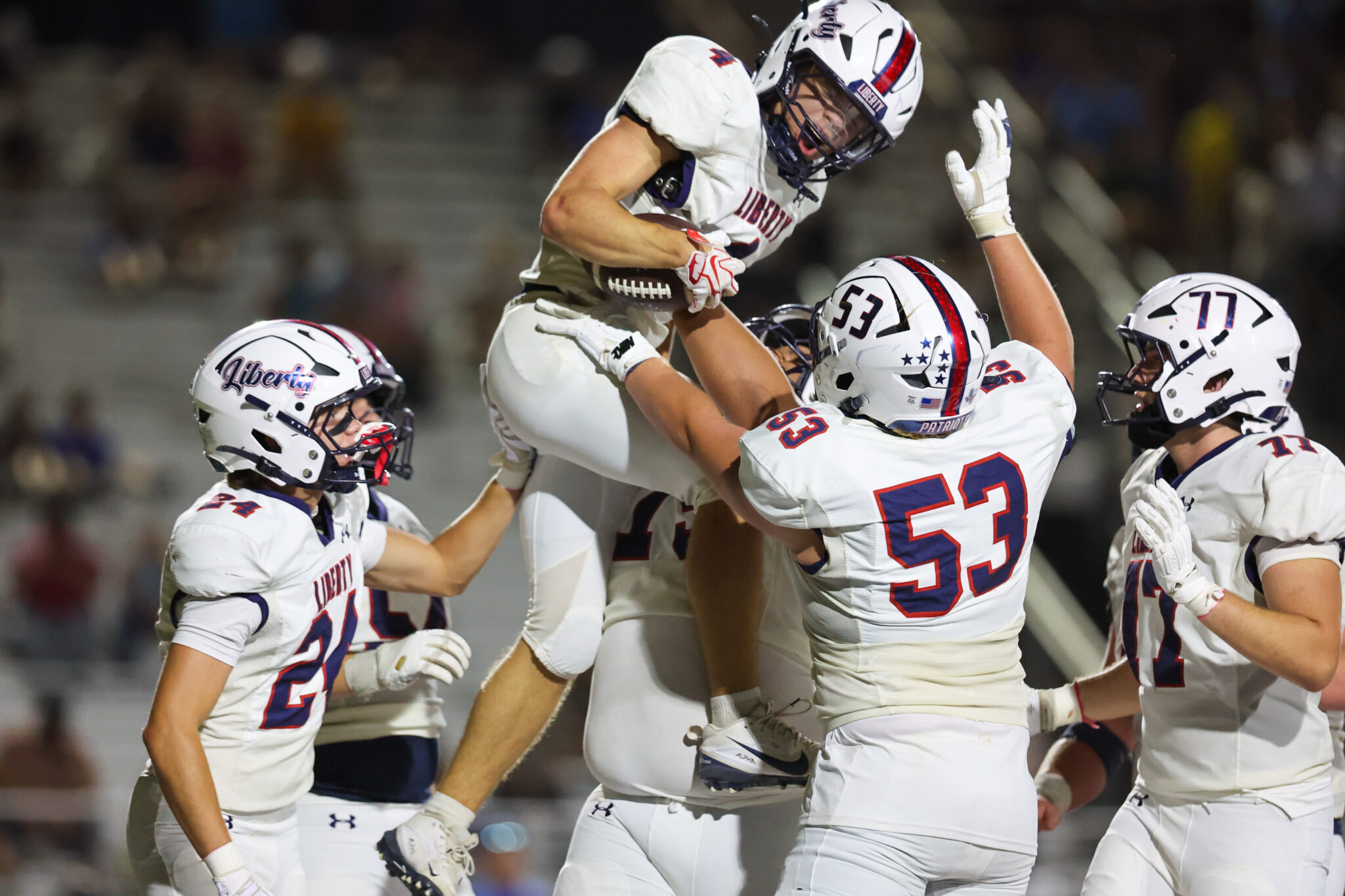 Seabolt Chase-18352 | Press Pass Sports Liberty University football players in white uniforms celebrate a teammate being lifted in the air on the field.