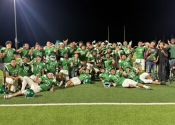 IMG_6943 | Press Pass Sports Group of football players in green uniforms posing on a field at night, with goalposts in the background and stadium lights overhead.
