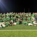 IMG_6943 | Press Pass Sports Group of football players in green uniforms posing on a field at night, with goalposts in the background and stadium lights overhead.