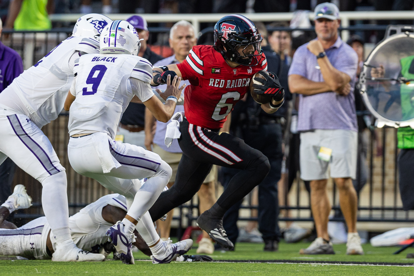 Tech-Abilene-FB-19 | Press Pass Sports American football player in red jersey (No. 6) runs with the ball as white-clad defenders close in on the field goal line.