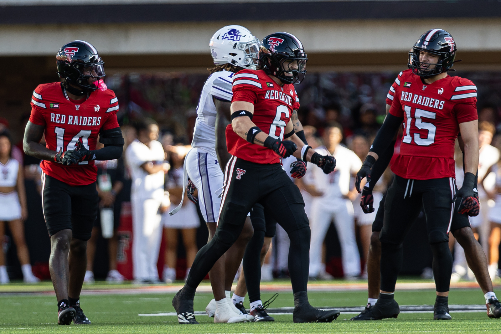 Tech-Abilene-FB-5 | Press Pass Sports Red Raiders players in red uniforms stand on the field during a game, focused and ready for action.