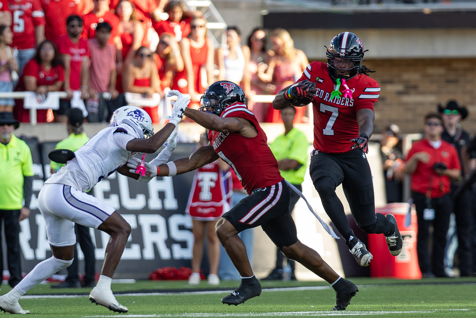 Tech-Abilene-FB-6 | Press Pass Sports Texas Tech Red Raiders player #7 runs with the ball while a white-uniform defender reaches in from the left; red-clad crowd in background.