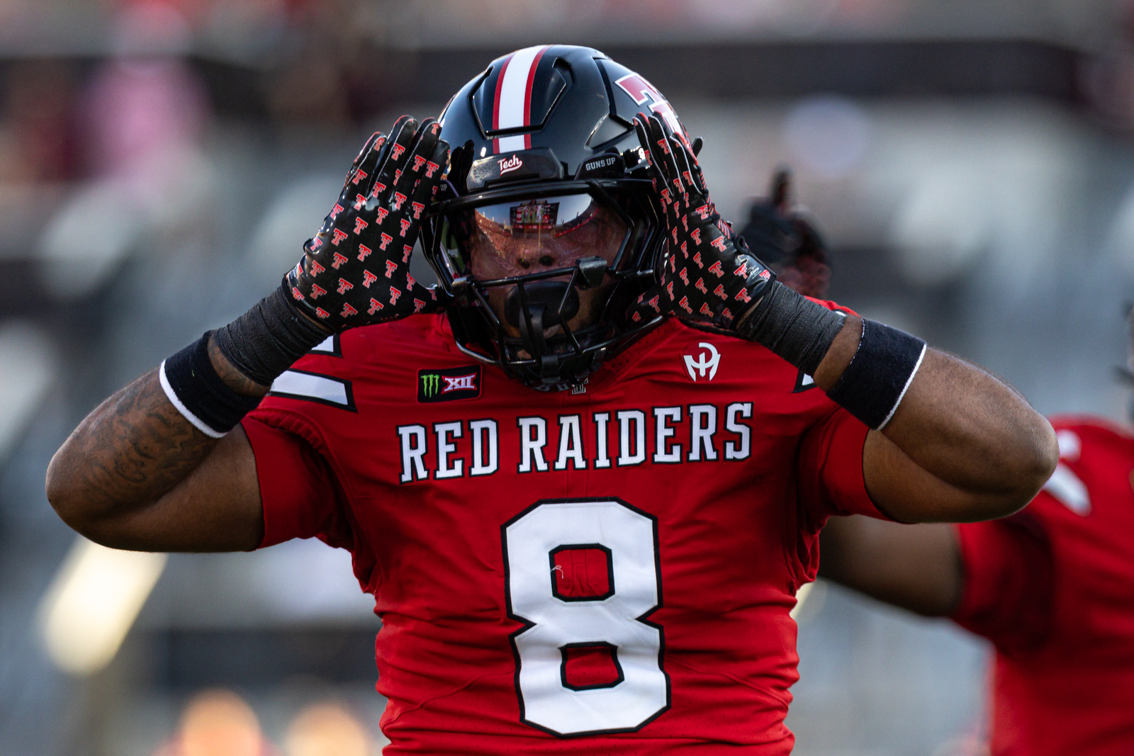 Tech-Abilene-FB-10 | Press Pass Sports Texas Tech Red Raiders football player wearing number 8 jersey raises his arms in celebration with a helmet on and gloves on both hands above head office.