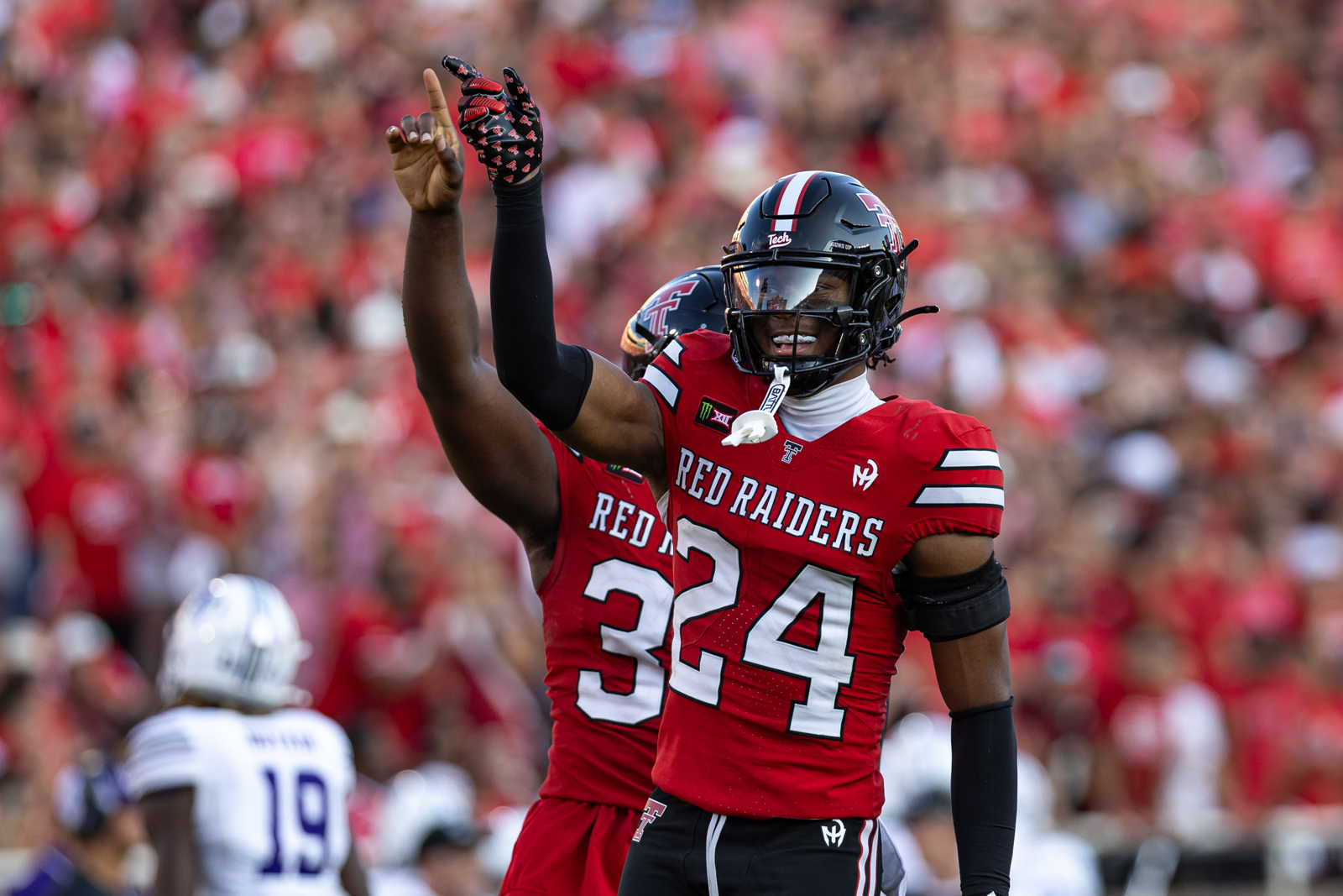 Tech-Abilene-FB-11 | Press Pass Sports Texas Tech Red Raiders player #34 raises his arm in celebration on the field with a packed red-clad crowd in the background.