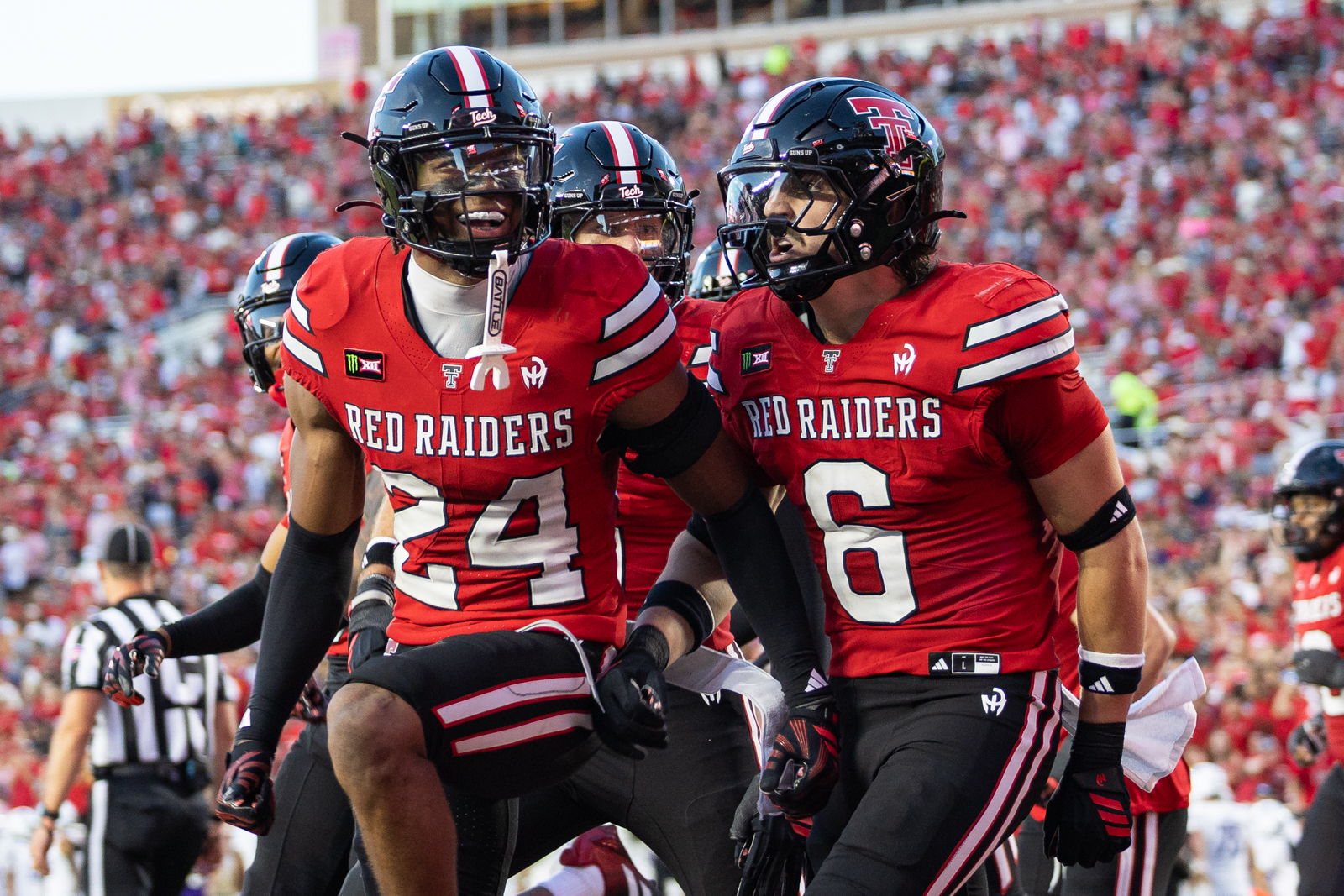 Tech-Abilene-FB-18 | Press Pass Sports Two Texas Tech Red Raiders football players in red jerseys celebrate on the field with a packed stadium behind them.