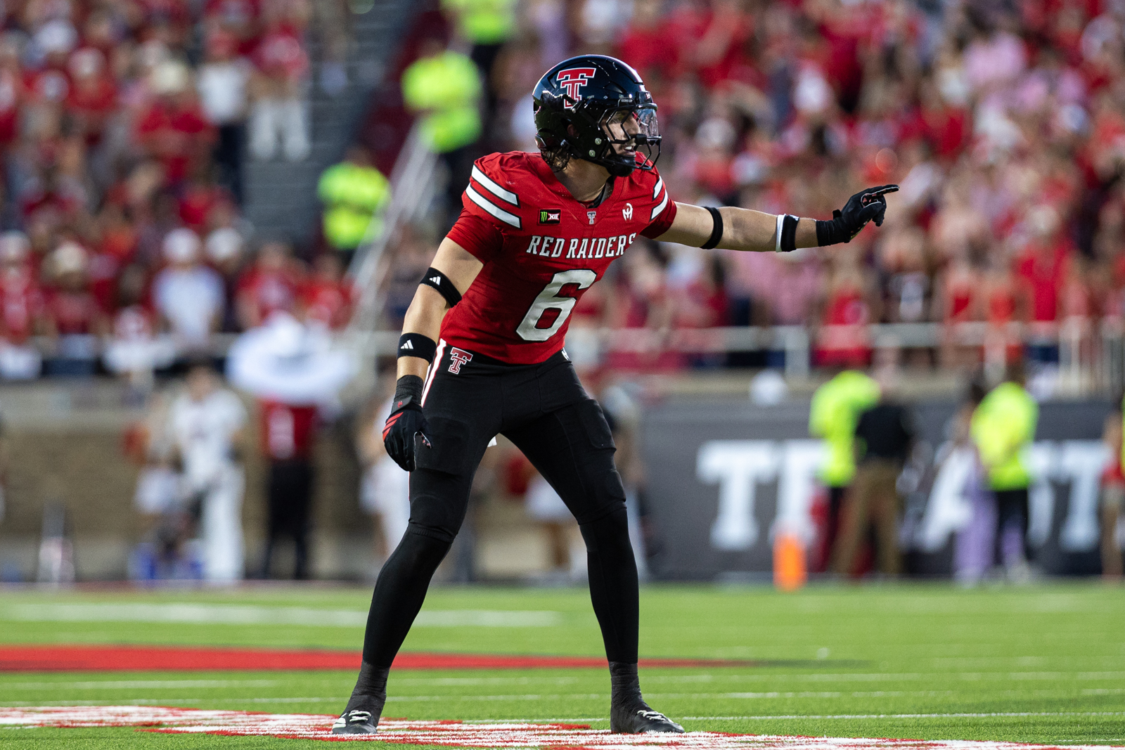 Tech-Abilene-FB-21 | Press Pass Sports Texas Tech Red Raiders football player wearing #6 points or signaling on the field during a game while the crowd watches in the stands at a stadium.