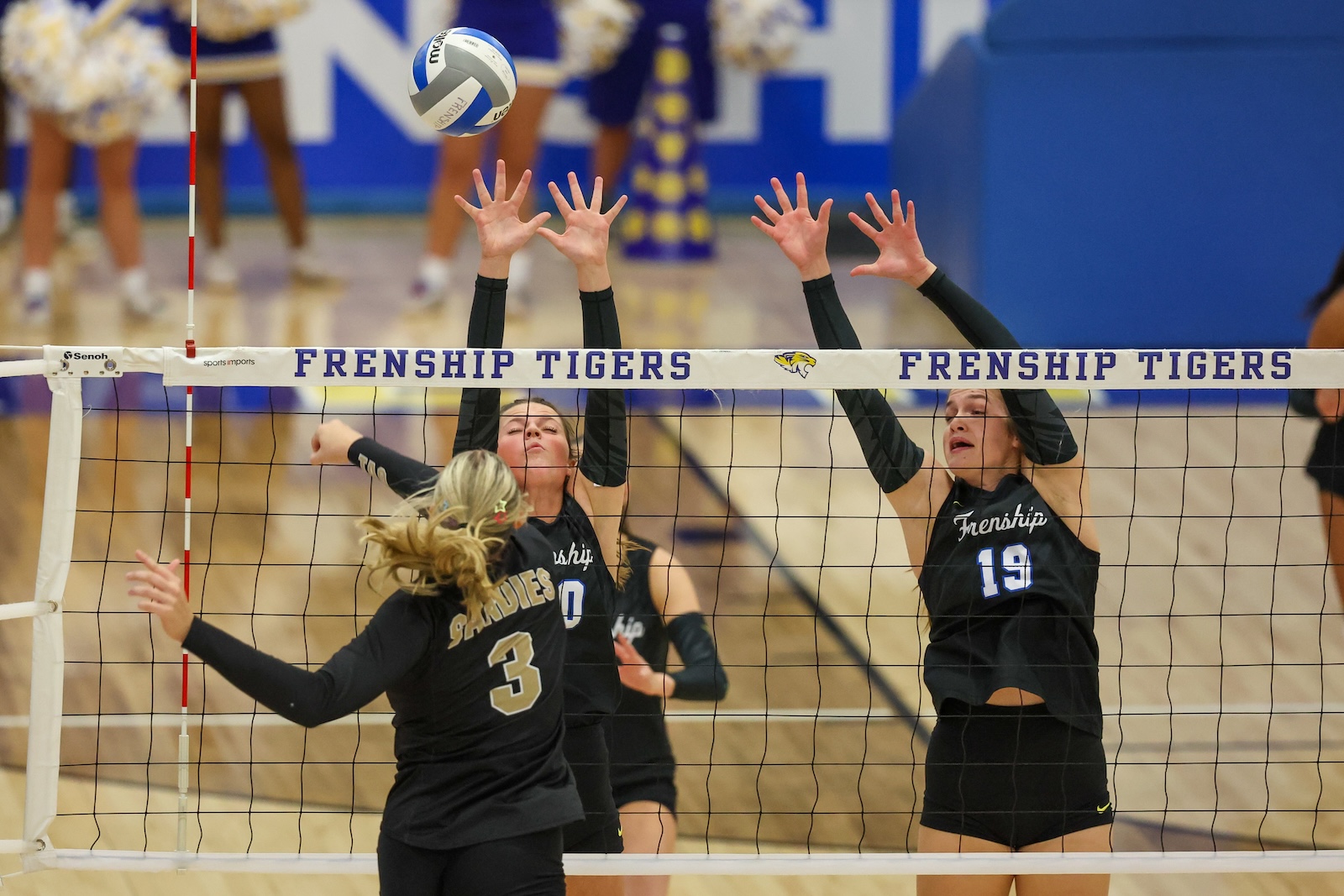 Seabolt Chase-11729 | Press Pass Sports Two Frenship Tigers players in black uniforms jump to block a ball at the net as a teammate approaches from the left; ball rising above the net.