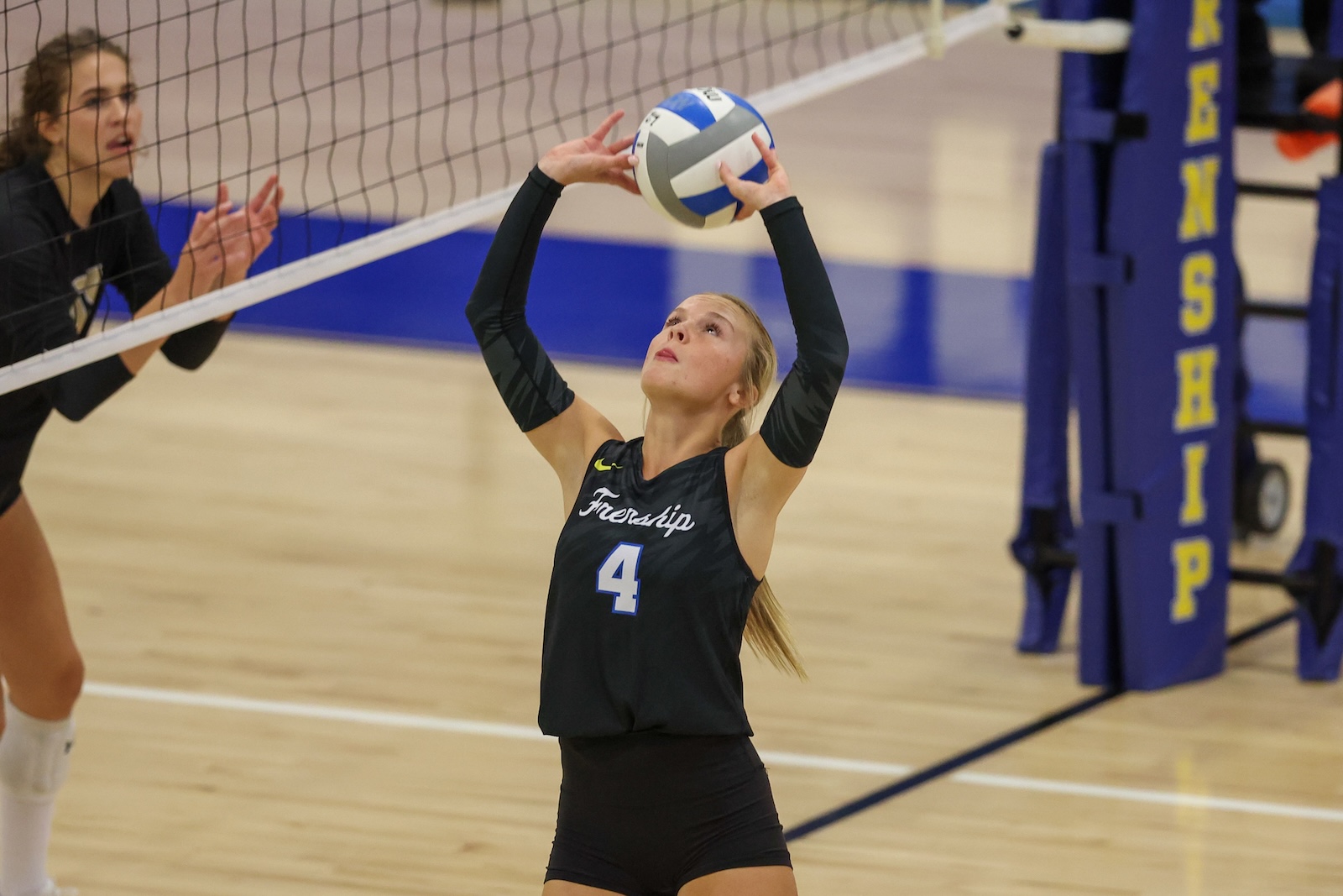 Seabolt Chase-12121 | Press Pass Sports Female volleyball player wearing #4 in a black jersey sets the ball above her head near the net in a match.