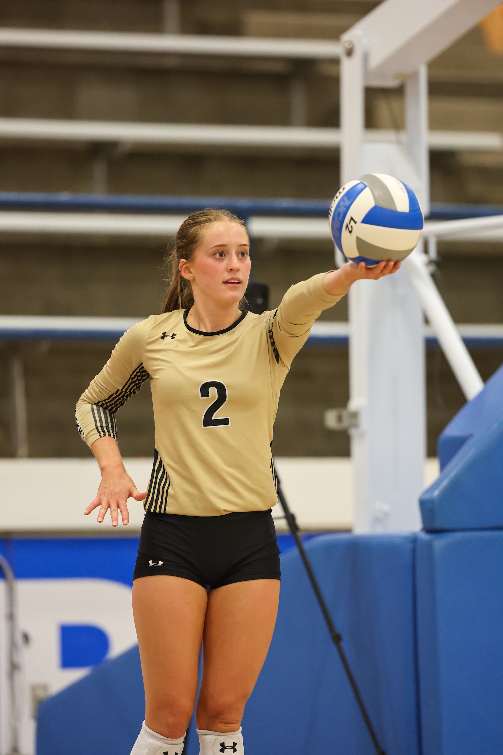 Seabolt Chase-12532 | Press Pass Sports Female volleyball player wearing a beige jersey with number 2, about to serve the ball indoors, arm extended to the right.