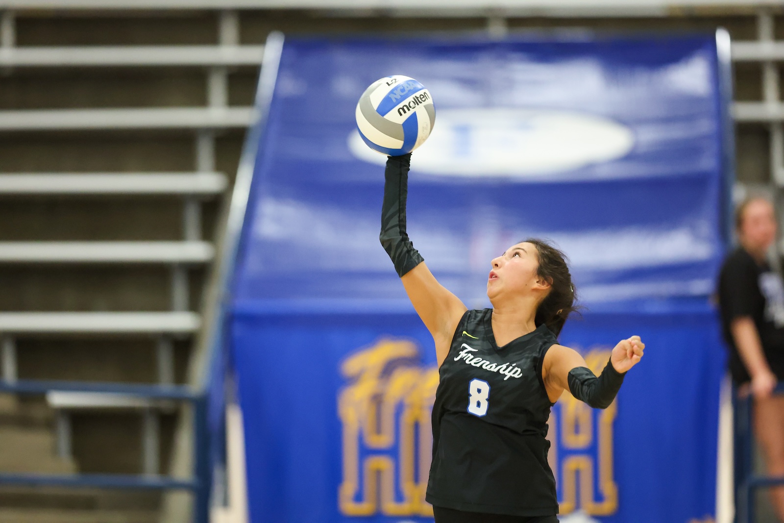 Seabolt Chase-12692 | Press Pass Sports Female volleyball player in a black jersey (#8) jumps to spike a white-blue ball indoors on a blue-court backdrop.