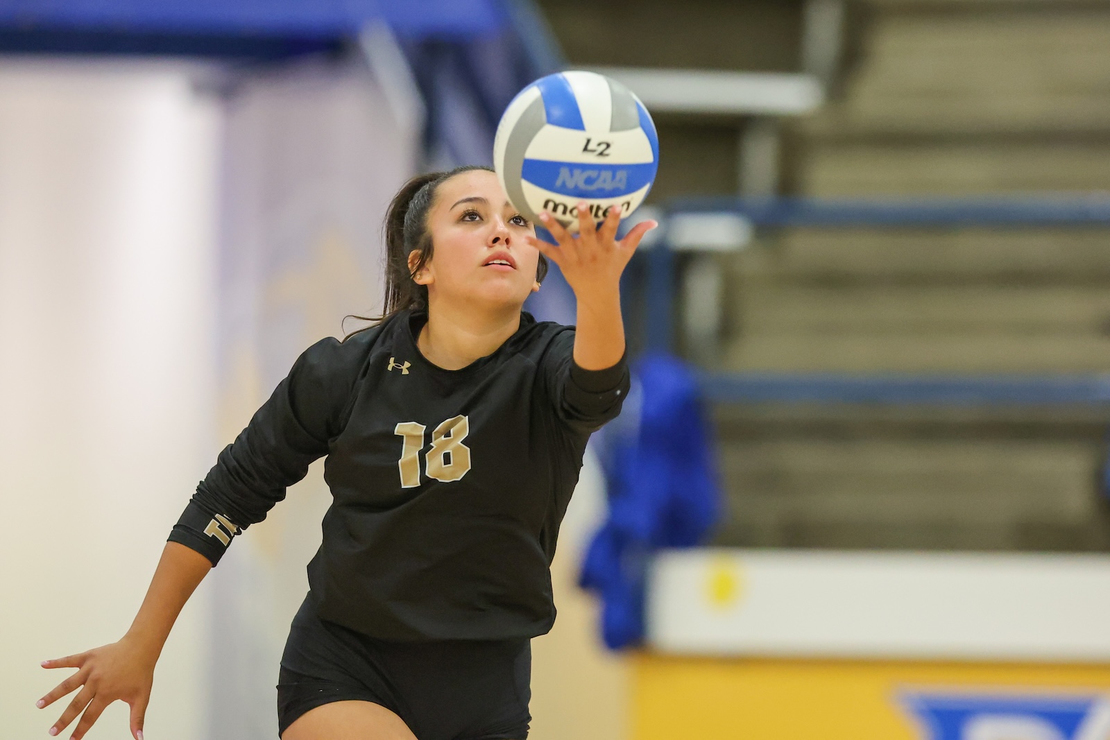 Seabolt Chase-12714 | Press Pass Sports Female volleyball player in a black jersey reaching to set/receive a ball in an indoor gym; jersey number 18 visible.