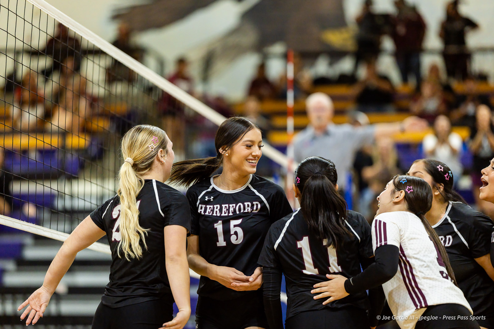 herford-vs-canyon-volleyball-jpegJoe-pps-3 | Press Pass Sports Hereford volleyball players in black uniforms celebrate together on the court near the net, smiling and hugging after a point.
