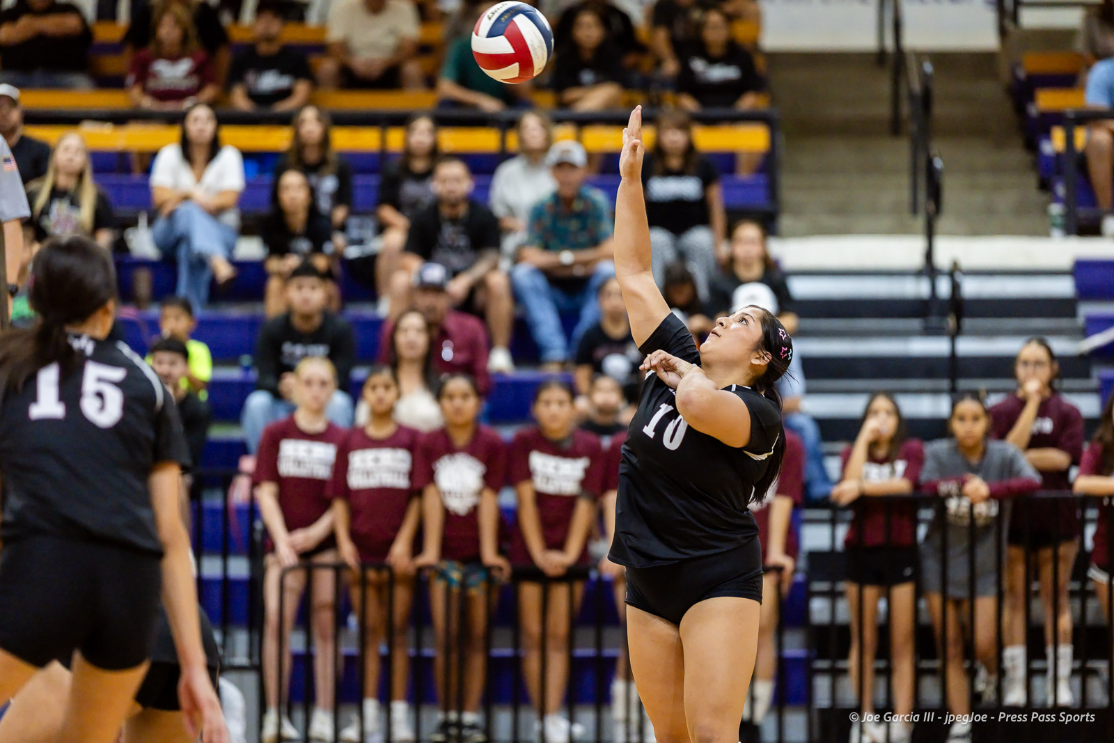herford-vs-canyon-volleyball-jpegJoe-pps-6 | Press Pass Sports Female volleyball player in black jersey #10 serves the ball overhead during a match, crowd watching in the stands behind a barrier.