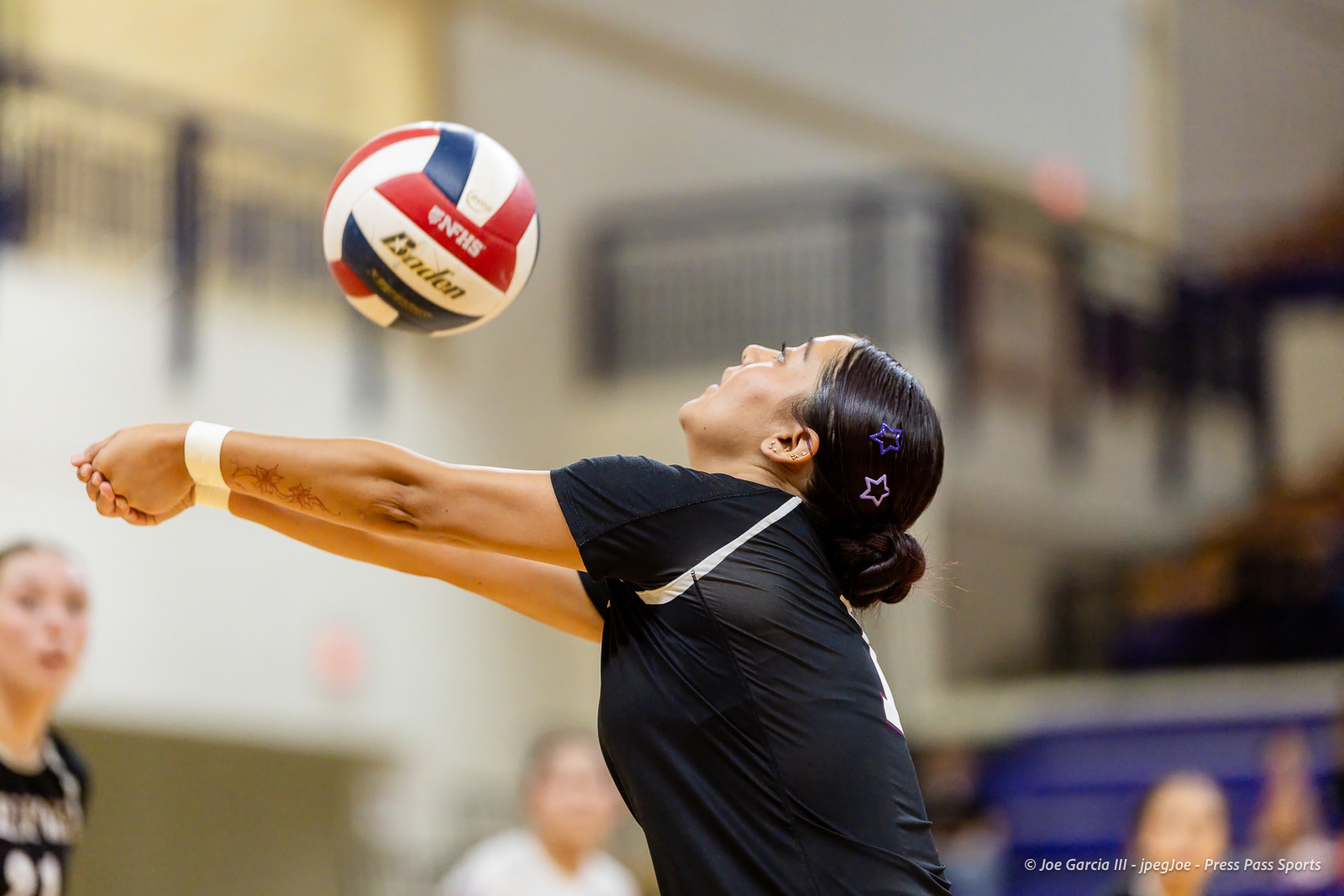 herford-vs-canyon-volleyball-jpegJoe-pps-14 | Press Pass Sports Volleyball player in black jersey dives forward with arms extended to receive a ball in an indoor gym, hair tied with star clips.