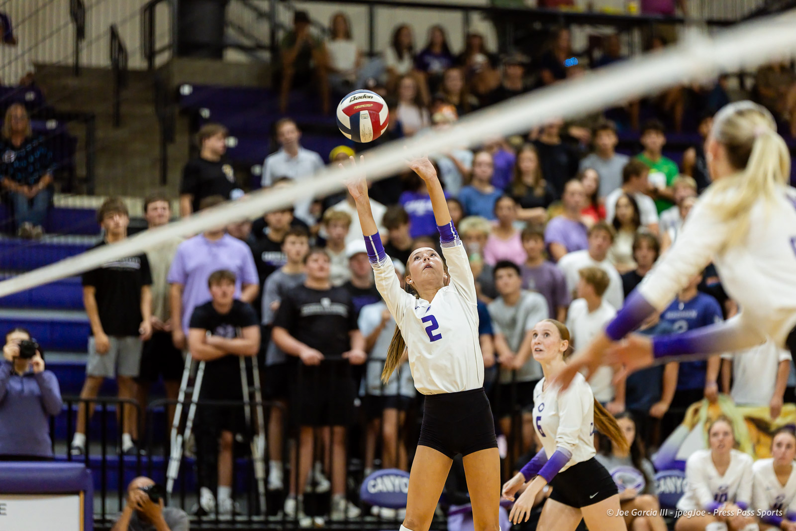 herford-vs-canyon-volleyball-jpegJoe-pps-16 | Press Pass Sports Female volleyball player in white jersey with number 2 sets the ball over the net as teammates and a crowded gym look on.