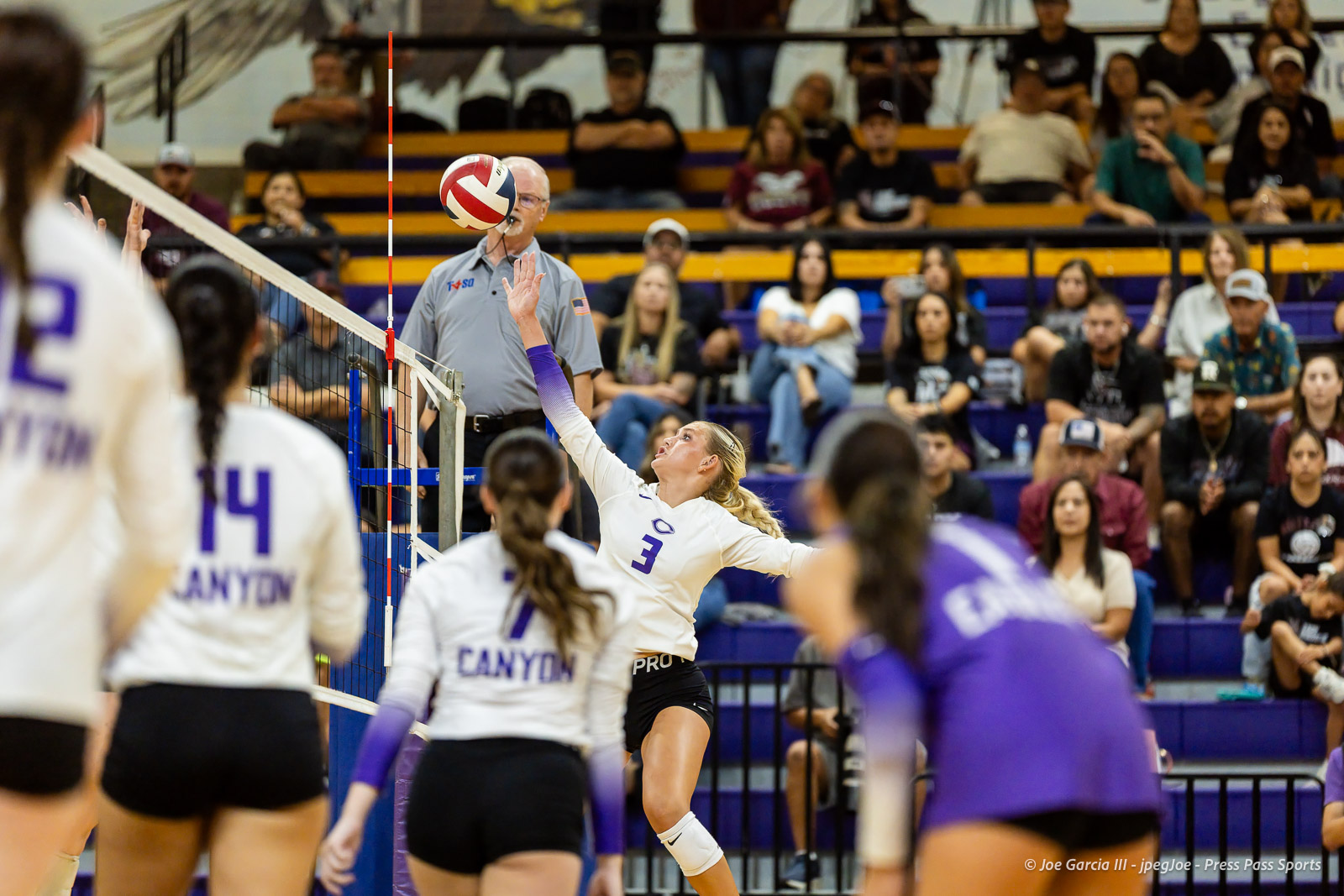 herford-vs-canyon-volleyball-jpegJoe-pps-22 | Press Pass Sports Volleyb all player in white #3 spikes the ball at the net during a match; spectators in bleachers watch.