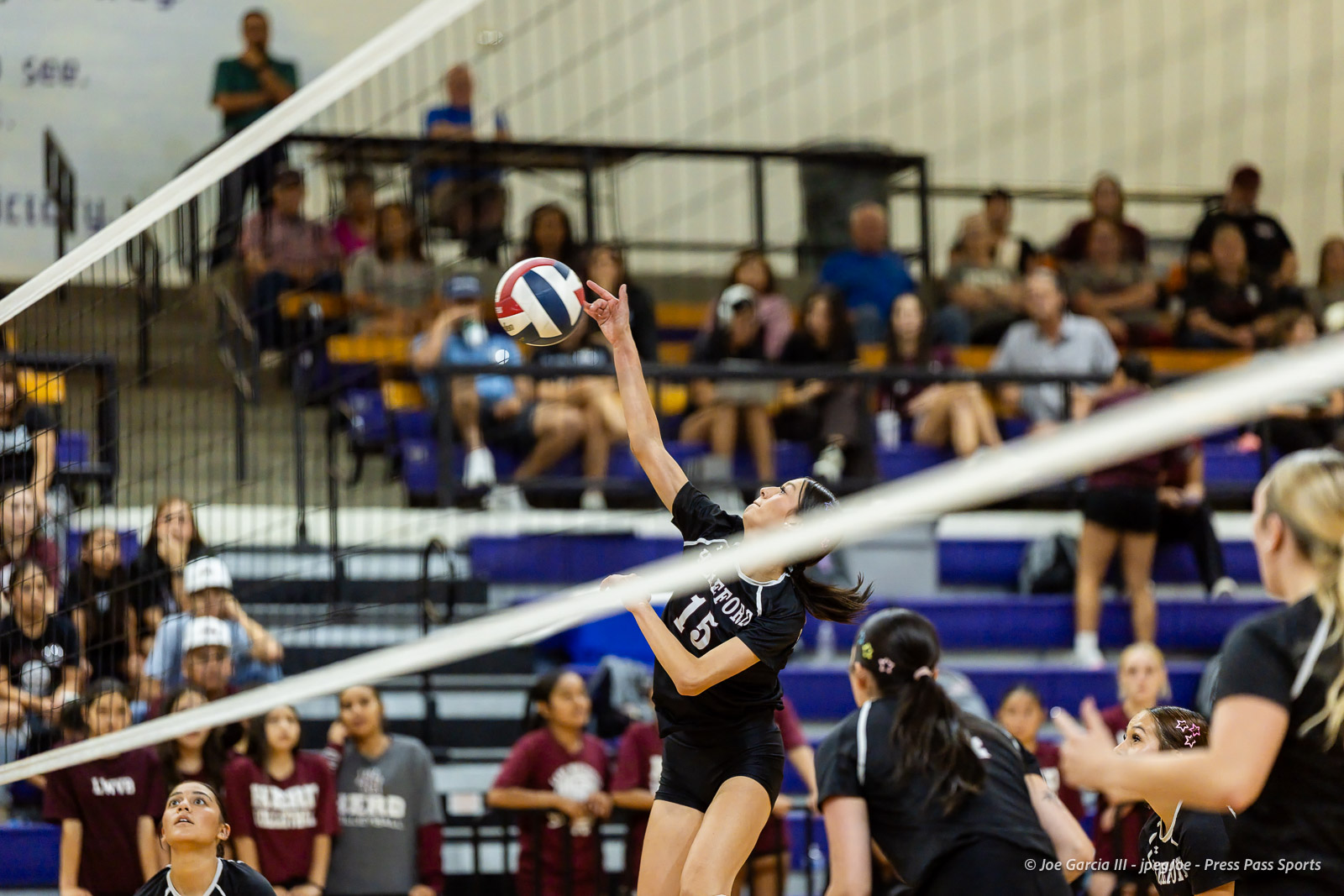 herford-vs-canyon-volleyball-jpegJoe-pps-25 | Press Pass Sports Female volleyball player in a black uniform spikes the ball over the net as spectators watch in the stands.