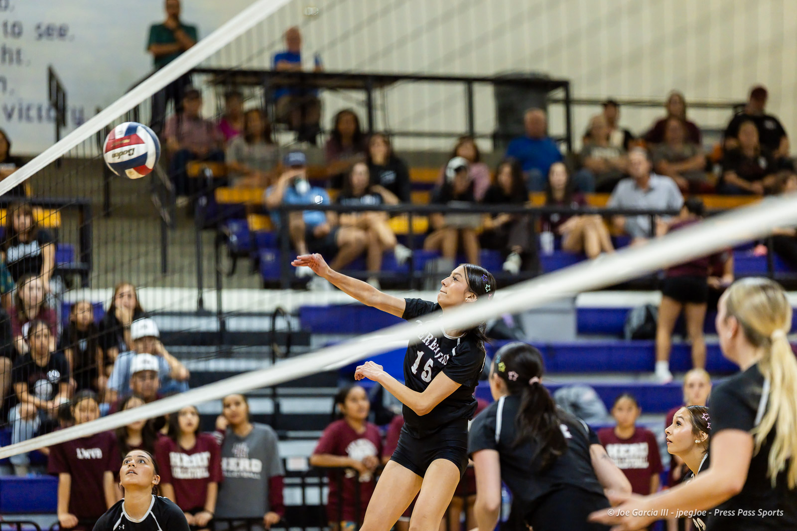 herford-vs-canyon-volleyball-jpegJoe-pps-26 | Press Pass Sports Female volleyball player hitting the ball over the net during a match, jumping mid-air with spectators in the bleachers behind her