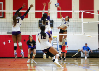 Edit 3 | Press Pass Sports Hard spike at the net by a player in white jersey as opponents block at the net; teammates nearby on the court.