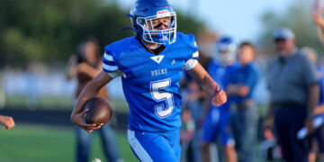 A football player in a blue uniform with the ball, sprinting on a field during a game.