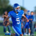 A football player in a blue uniform with the ball, sprinting on a field during a game.