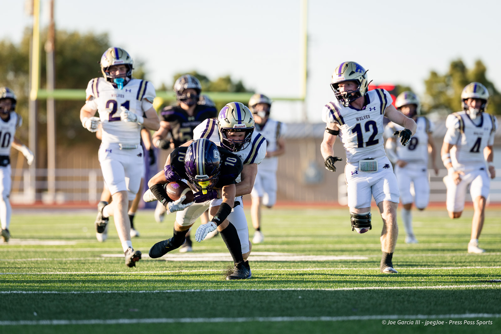 dalhart-vs-panhandle-football-jpegJoe-pps-1 | Press Pass Sports Purple-uniform football player runs with the ball as a white-uniform defender tackles him on a sunny field surrounded by teammates and players from both teams.