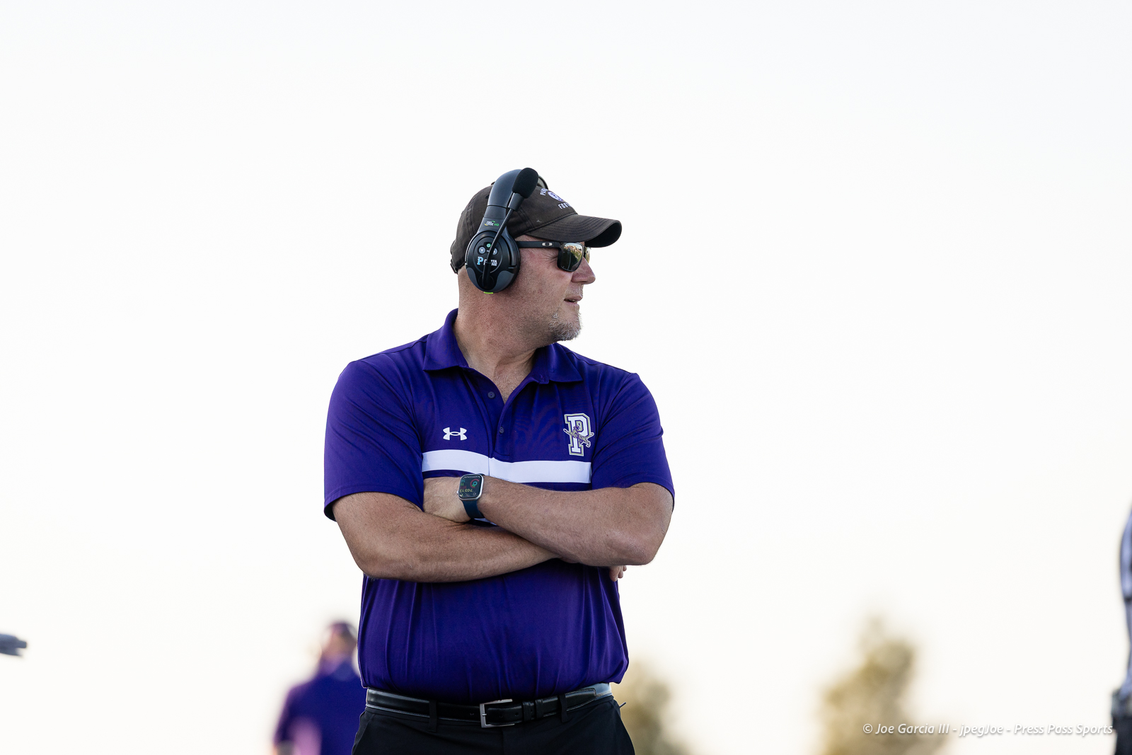 dalhart-vs-panhandle-football-jpegJoe-pps-2 | Press Pass Sports Coach wearing a purple polo and headset, arms crossed, looking to the right outdoors.