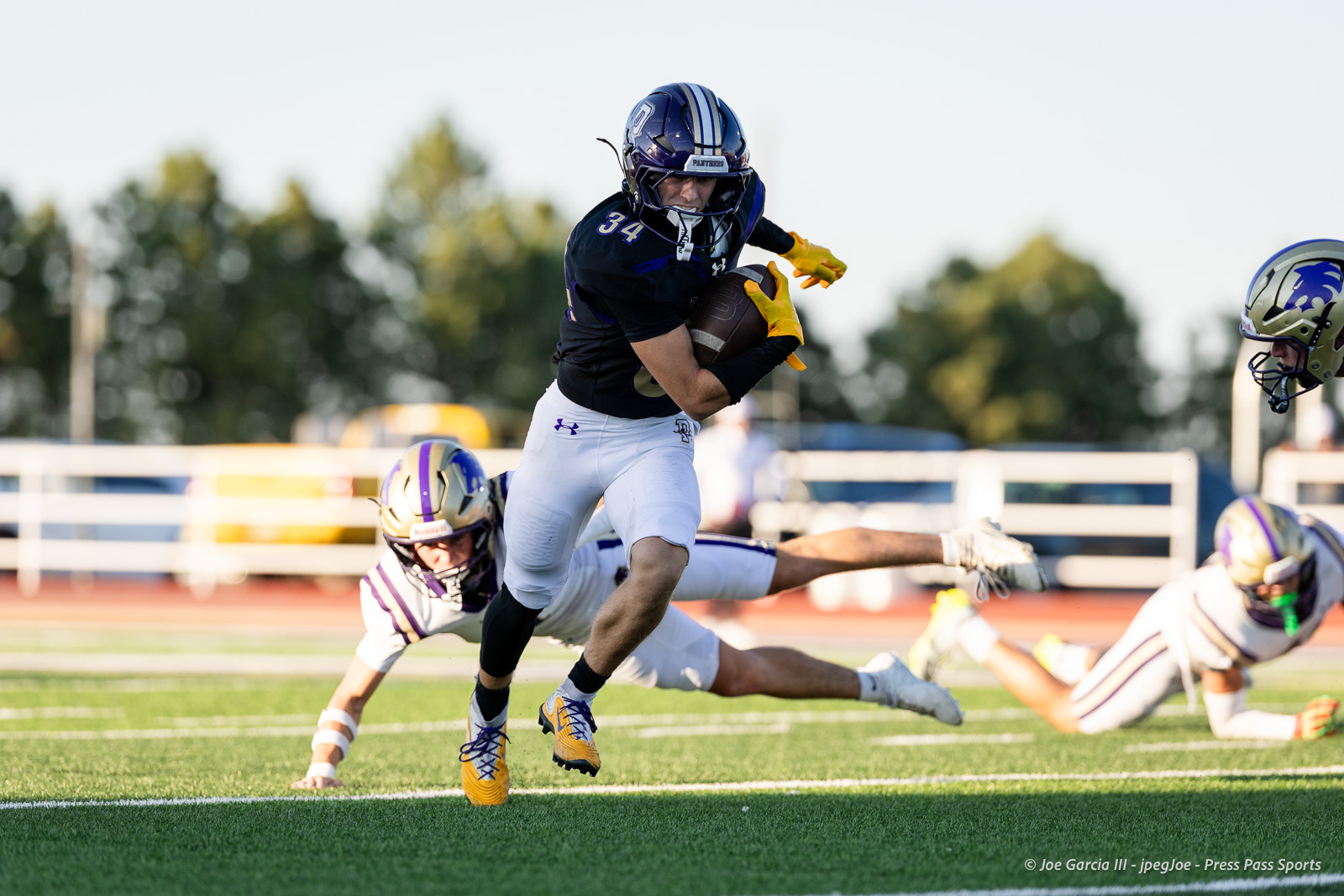 dalhart-vs-panhandle-football-jpegJoe-pps-3 | Press Pass Sports Young football player in a dark jersey with the ball, sprinting down the field while defenders dive behind him on a green turf field.
