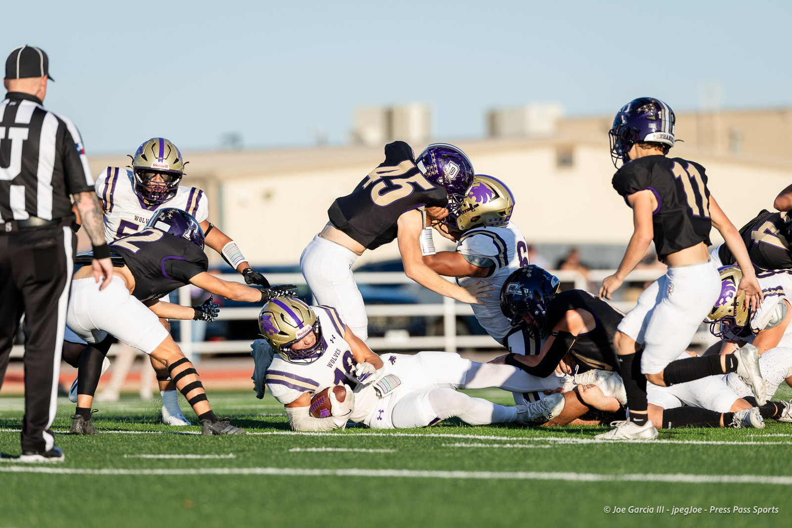 dalhart-vs-panhandle-football-jpegJoe-pps-5 | Press Pass Sports Varsity football game action: players in purple-gold and white collide as a tackle unfolds on the grassy field common in high school football