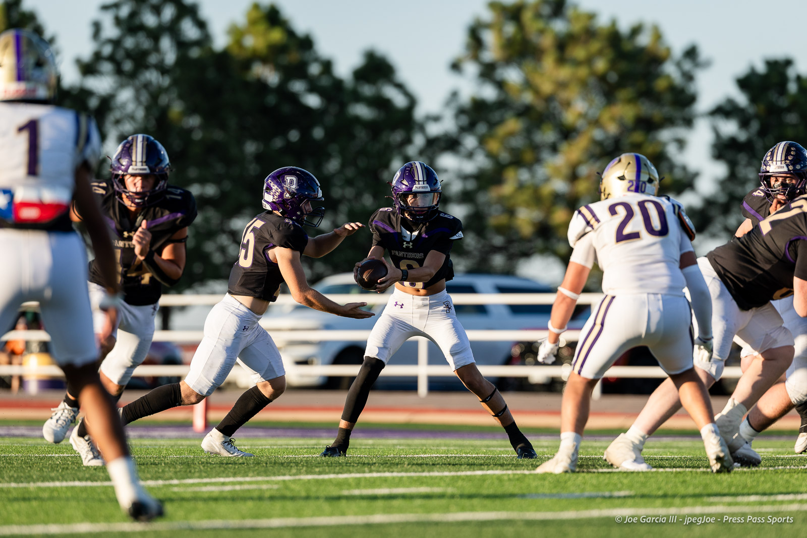 dalhart-vs-panhandle-football-jpegJoe-pps-7 | Press Pass Sports Quarterback in a black jersey with the ball, backed by blockers, as teammates rally on a green football field.