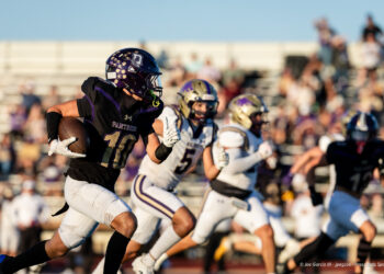 dalhart-vs-panhandle-football-jpegJoe-pps-14 | Press Pass Sports Football player wearing black and purple Panthers uniform with the ball racing down the field as defenders pursue, stands full of spectators in the background.