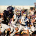 dalhart-vs-panhandle-football-jpegJoe-pps-14 | Press Pass Sports Football player wearing black and purple Panthers uniform with the ball racing down the field as defenders pursue, stands full of spectators in the background.