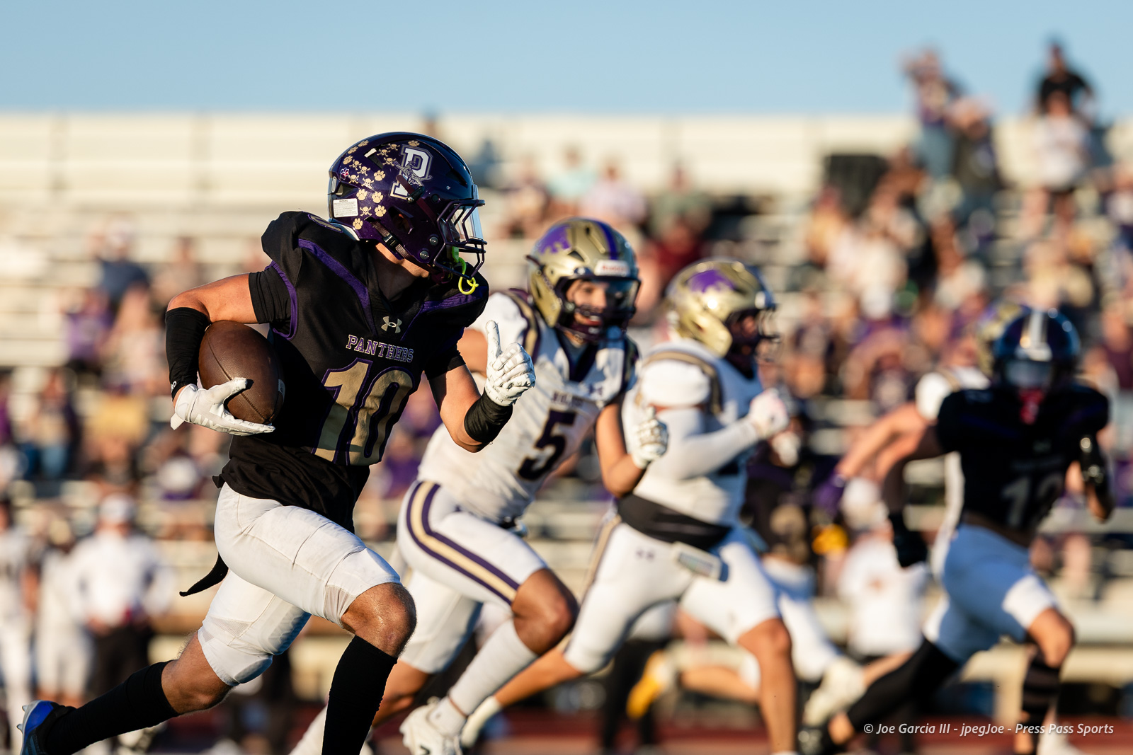 dalhart-vs-panhandle-football-jpegJoe-pps-14 | Press Pass Sports Football player wearing black and purple Panthers uniform with the ball racing down the field as defenders pursue, stands full of spectators in the background.