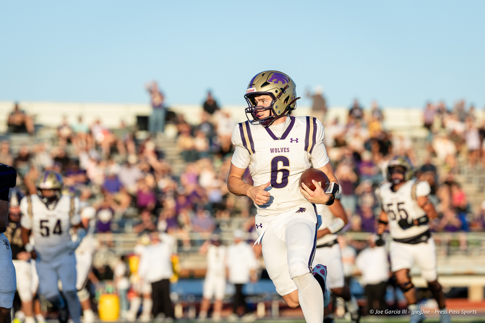 dalhart-vs-panhandle-football-jpegJoe-pps-16 | Press Pass Sports Football player in white and purple Wolves jersey #6 running with ball during a game; crowd in stands behind.