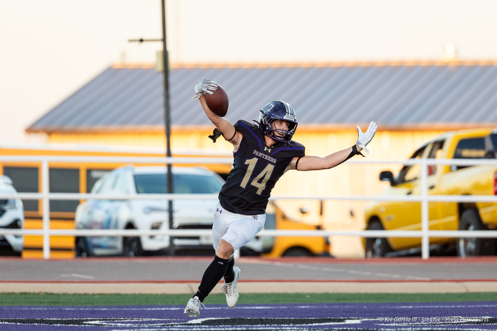 dalhart-vs-panhandle-football-jpegJoe-pps-21 | Press Pass Sports Football player wearing number 14 in a black Panthers uniform reaches for a pass with arms outstretched on a purple turf field.